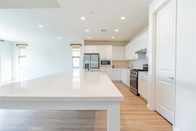 a large white kitchen with kitchen island a sink a stove a refrigerator and white cabinets next to a window