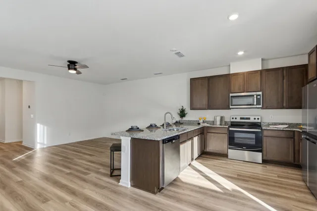 a kitchen with stainless steel appliances granite countertop a stove top oven a sink dishwasher and a refrigerator with wooden floor