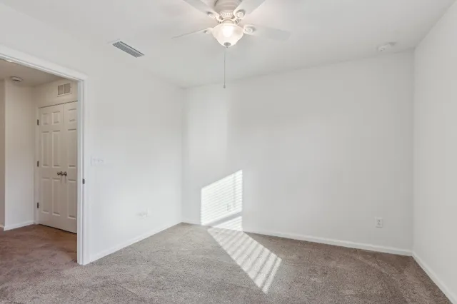 an empty room with chandelier fan and windows