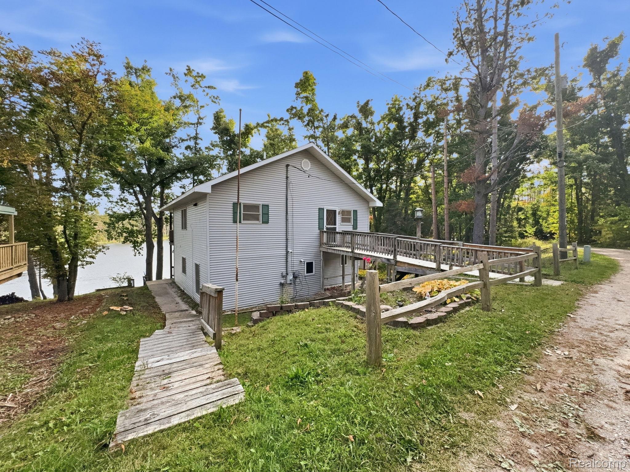 2259 Kassuba Road Gaylord, MI 49735 - Photo 33 of 46 Two-story residence with light-colored siding, a wooden ramp entrance, a split-rail fence, and mature trees
