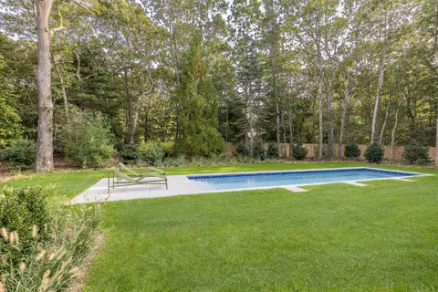 a view of a swimming pool with lawn chairs and large trees