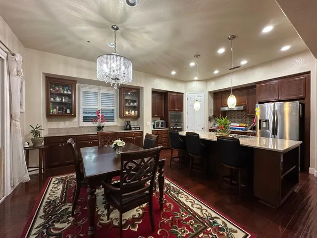 a kitchen with stainless steel appliances granite countertop a refrigerator a sink dishwasher a dining table and chairs with wooden floor