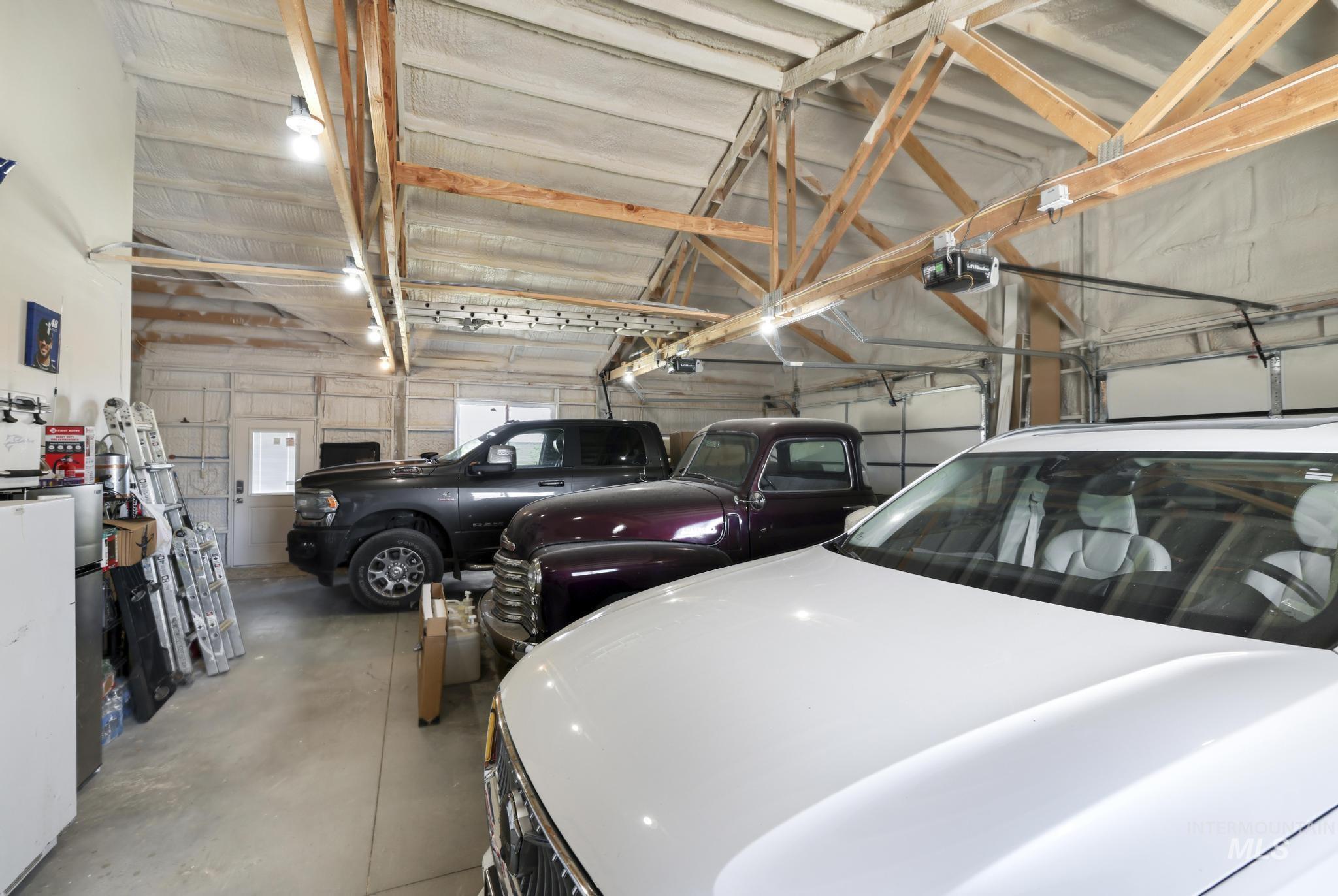 758 Cedar Crk Road Rogerson, ID 83302 - Photo 30 of 50 Spacious garage featuring exposed wooden truss ceiling, multiple overhead lighting fixtures, and three overhead garage doors