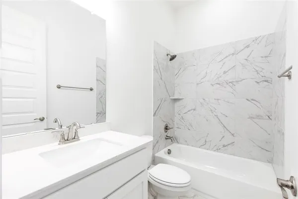 a bathroom with a granite countertop bathtub shower sink vanity mirror and toilet