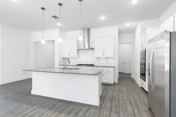 a kitchen with stainless steel appliances granite countertop a sink a stove a refrigerator and island with wooden floor