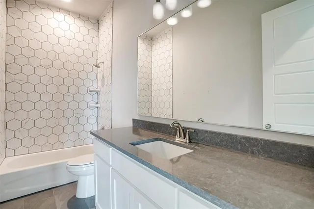 a bathroom with a granite countertop bathtub sink vanity mirror and toilet
