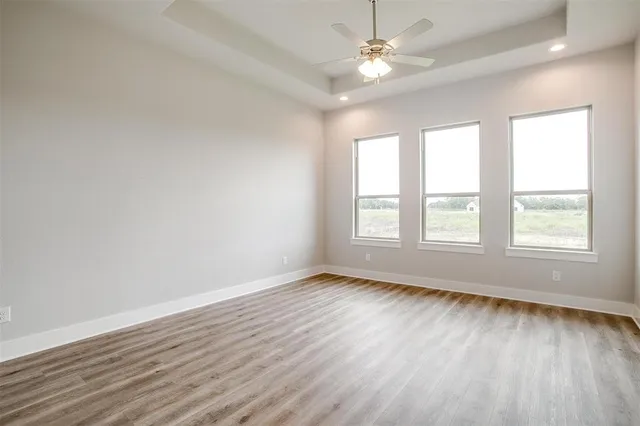 an empty room with wooden floor ceiling fan and windows