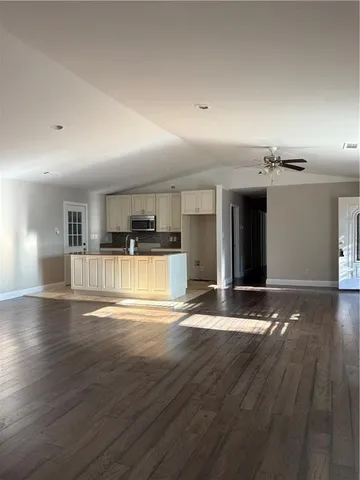 an empty room with wooden floor and kitchen view