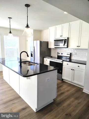 a kitchen with stainless steel appliances granite countertop a sink a stove a refrigerator and white cabinets