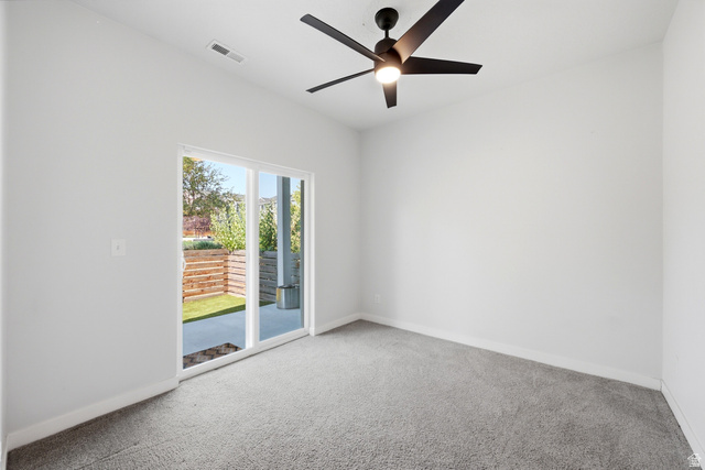 862 Founders Point Lane South Midvale, UT 84047 - Photo 5 of 45 Room featuring a ceiling fan, light gray carpeting, and a sliding glass door opening to an outdoor patio with a wood-slatted retaining wall and artificial turf