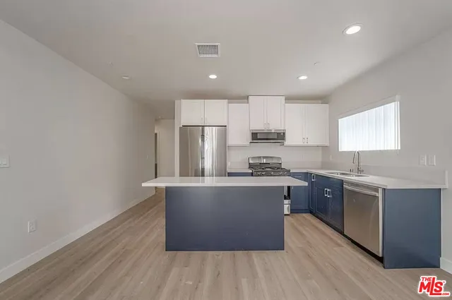 a large kitchen with stainless steel appliances granite countertop a stove a sink dishwasher a refrigerator and white cabinets with wooden floor