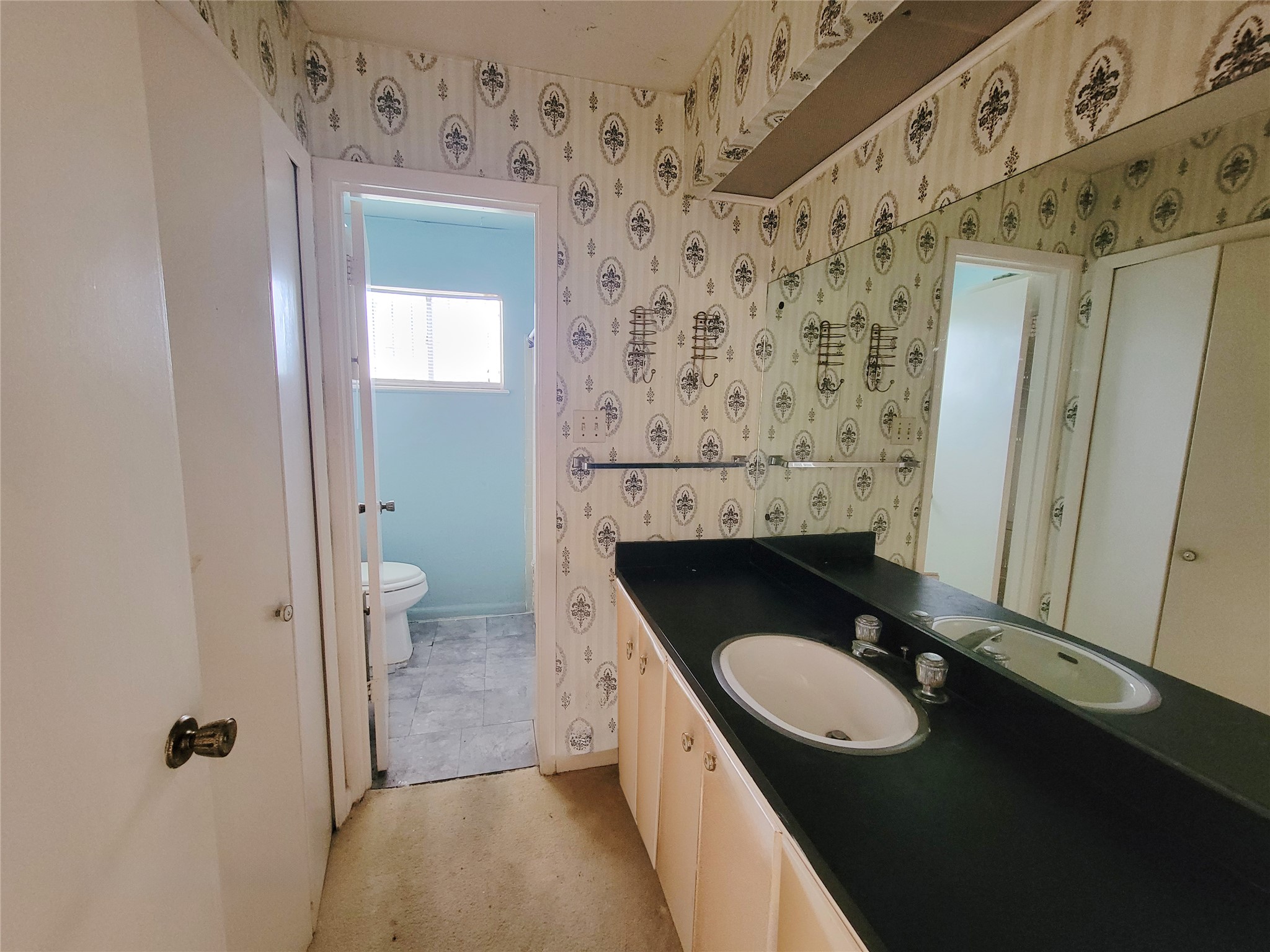 6605 Highpoint Drive Austin, TX 78723 - Photo 9 of 11 Bathroom featuring an integrated vanity with a single basin sink, a large wall-mounted mirror, and patterned wallpaper