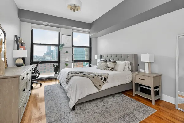 a bedroom with a bed and a large mirror on dresser next to a window