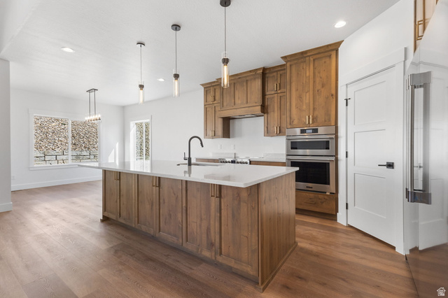 638 East Mountain Road North Ogden, UT 84414 - Photo 4 of 28 Kitchen featuring brown cabinetry, decorative light fixtures, stainless steel appliances, a kitchen island with sink, and dark wood-style flooring