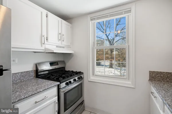 a kitchen with stainless steel appliances granite countertop white cabinets and a window