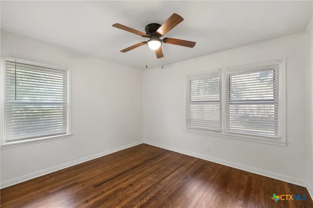 an empty room with wooden floor ceiling fan and window