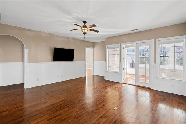 an empty room with wooden floor chandelier fan and windows