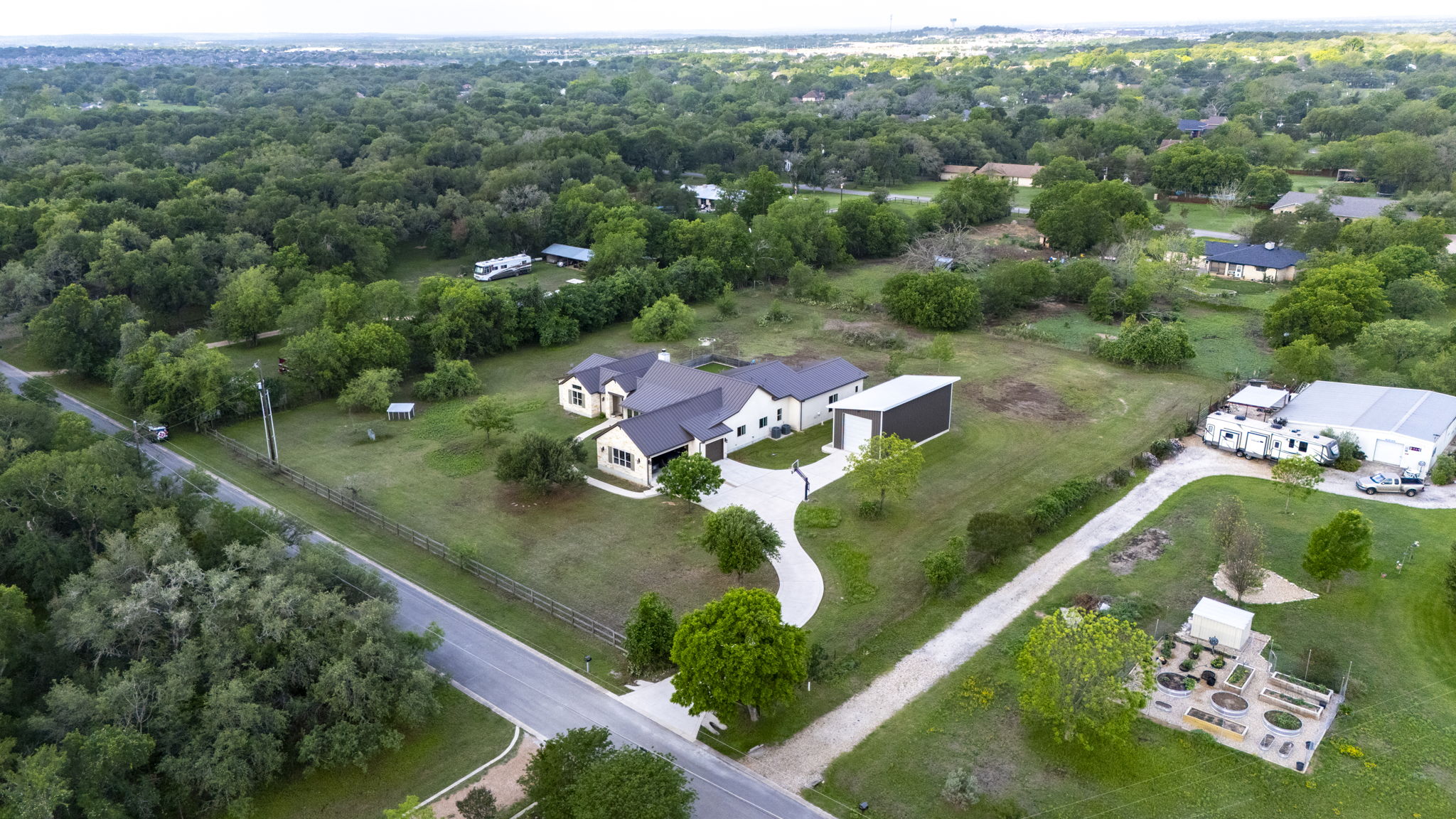 16202 Remuda Trail Buda, TX 78610 - Photo 37 of 40 The property features a spacious residence with a winding driveway, a detached garage, and a separate large outbuilding, all set within an expansive landscaped lot with mature trees