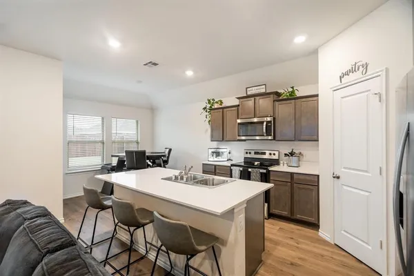 a kitchen with stainless steel appliances a stove a sink dishwasher a refrigerator white cabinets and wooden floor