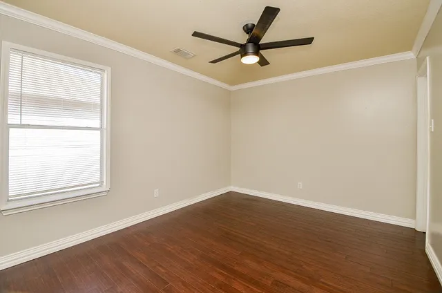 an empty room with wooden floor fan and windows