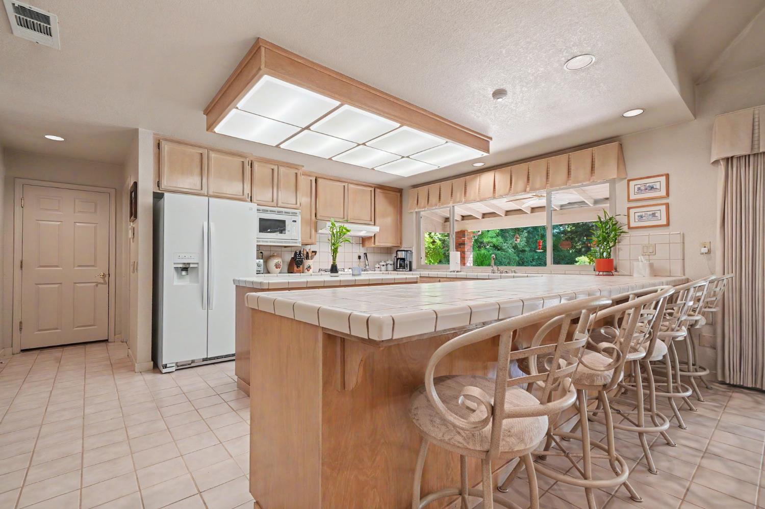9069 Bader Road Elk Grove, CA 95624 - Photo 14 of 70 Kitchen featuring extra eating area, light wood cabinetry, white tile countertops, and a white side-by-side refrigerator