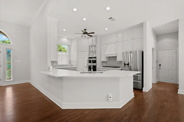 a large kitchen with stainless steel appliances a large counter top a stove a refrigerator white cabinets and wooden floor