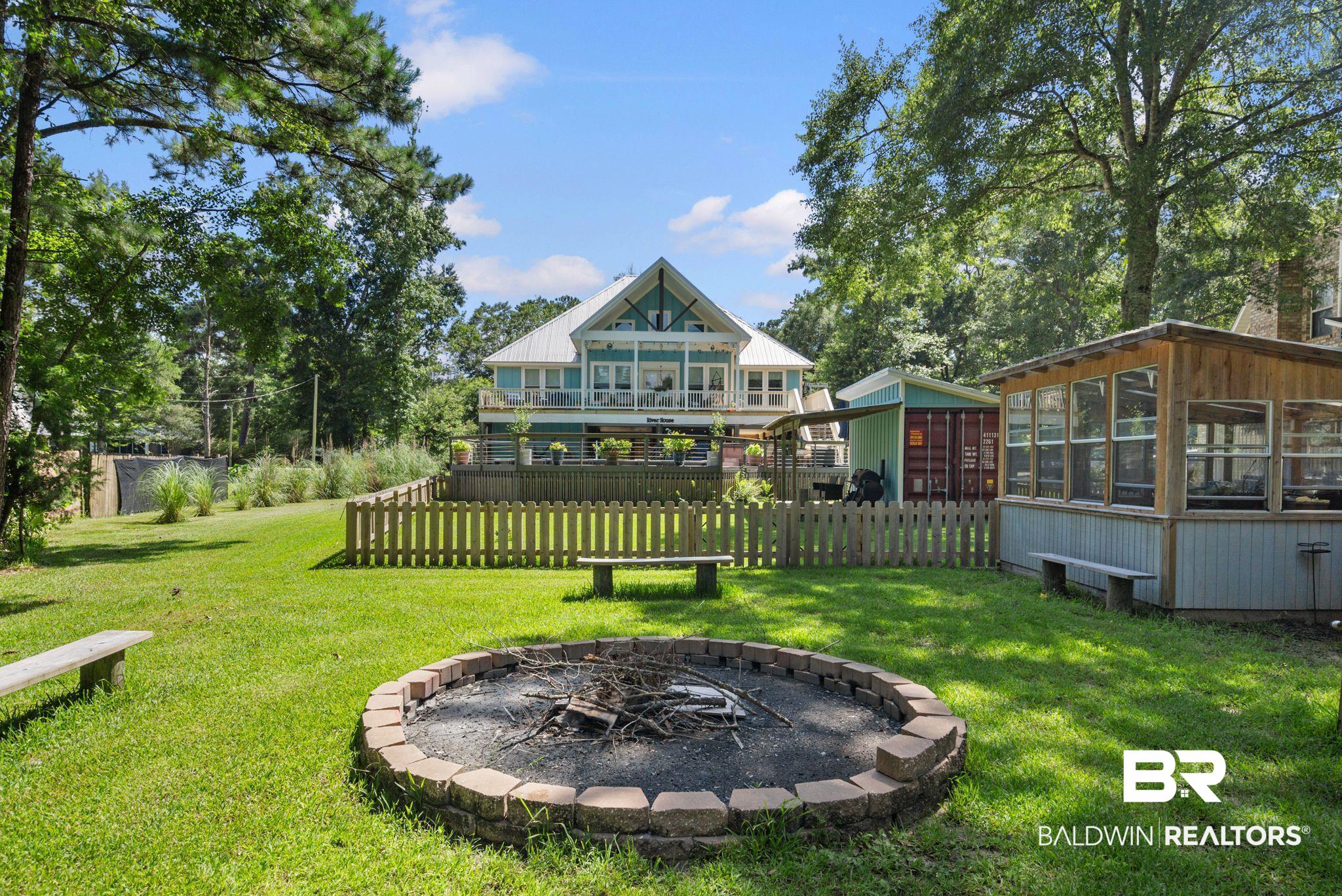 7266 Franklin Road Foley, AL 36535 - Photo 59 of 64 Expansive backyard featuring a stone-edged fire pit, a picket fence enclosing a deck, a separate screened structure, and a large central lawn area