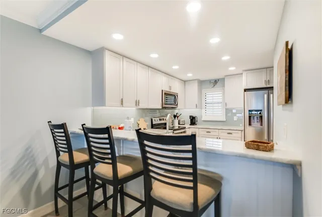 a kitchen with stainless steel appliances kitchen island granite countertop a dining table chairs and a refrigerator