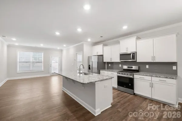 a large kitchen with stainless steel appliances granite countertop a stove top oven a sink a refrigerator and white cabinets with wooden floor