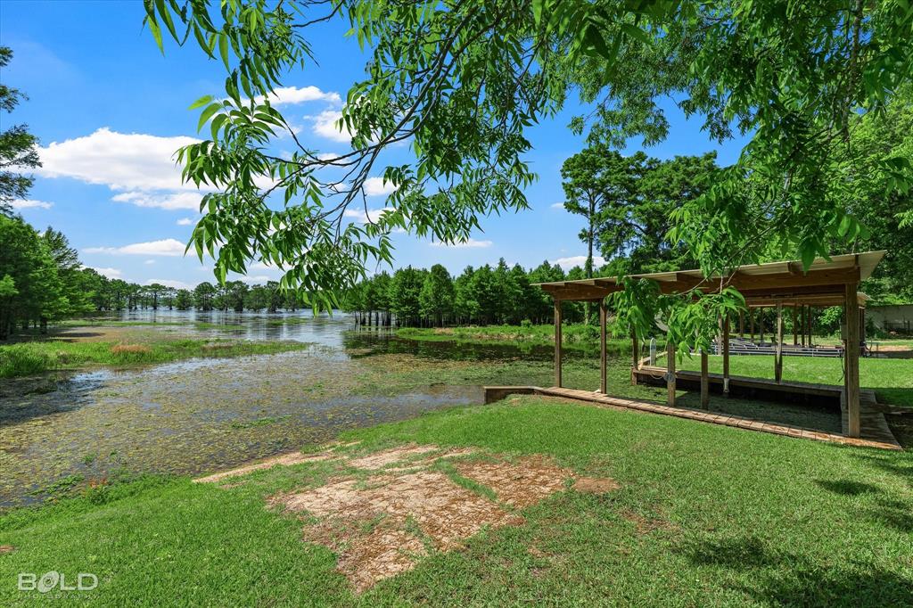225 Marie Road Ringgold, LA 71068 - Photo 5 of 40 Waterfront property featuring a wood-frame boat dock with a covered slip, lush green lawn, and mature trees