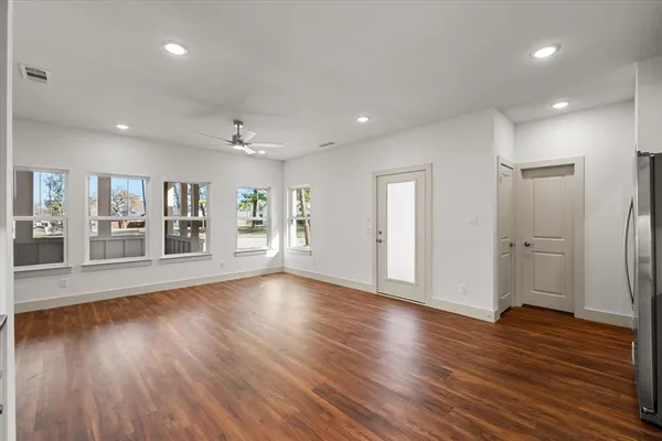 a view of an empty room with wooden floor and a kitchen