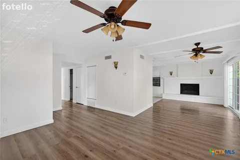 a view of an empty room with wooden floor and a ceiling fan