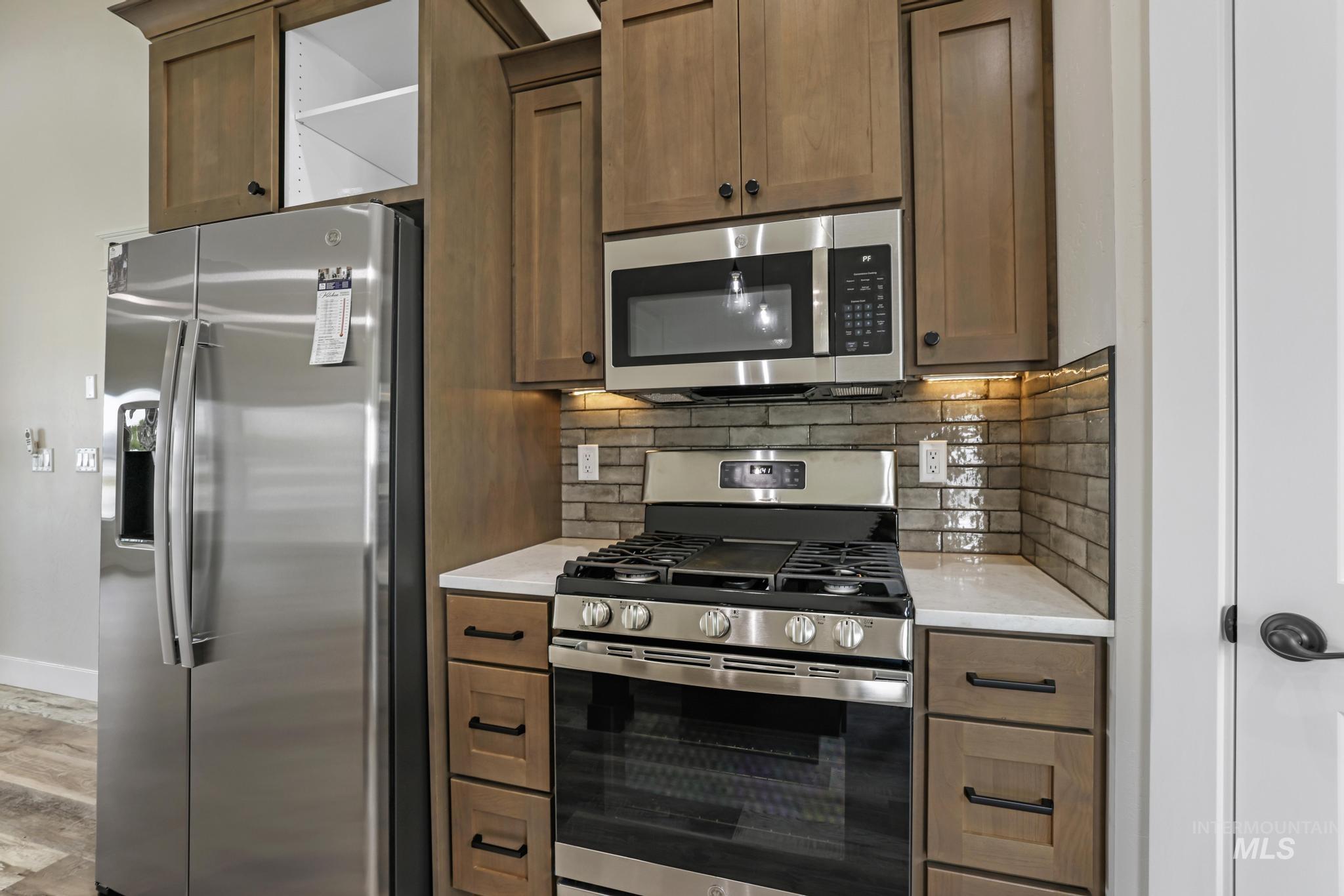 1441 Haizlee Way Twin Falls, ID 83301 - Photo 5 of 26 Kitchen with stainless steel appliances, backsplash, wood finish cabinets, light stone counters, and light wood finished floors