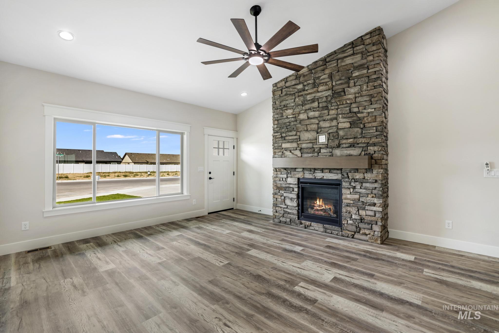1441 Haizlee Way Twin Falls, ID 83301 - Photo 7 of 26 Unfurnished living room featuring vaulted ceiling, light wood-style flooring, a ceiling fan, a stone fireplace, and recessed lighting