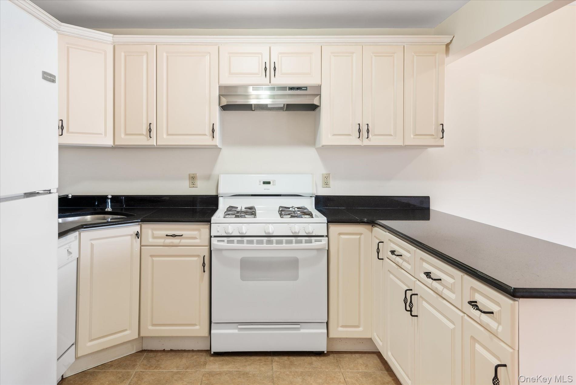 71-05 Cooper Avenue, Unit 2 Queens, NY 11385 - Photo 8 of 15 Kitchen featuring white appliances, under cabinet range hood, light tile patterned flooring, dark stone counters, and cream cabinets