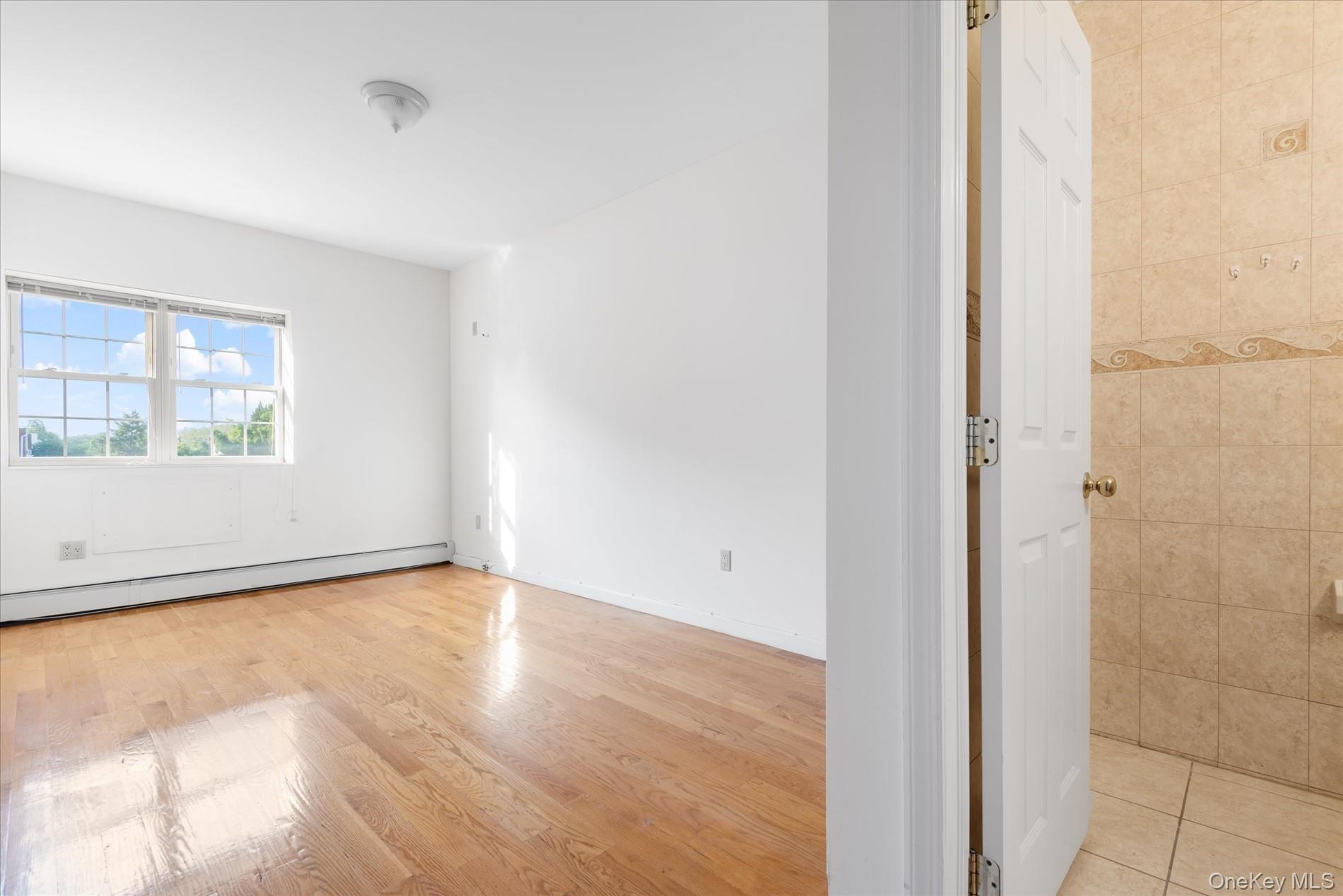 71-05 Cooper Avenue, Unit 2 Queens, NY 11385 - Photo 10 of 15 Empty room featuring a baseboard heating unit and light wood-style floors