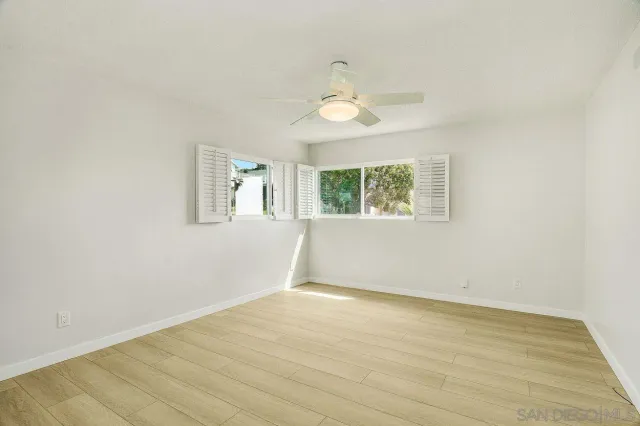 an empty room with wooden floor fan and windows