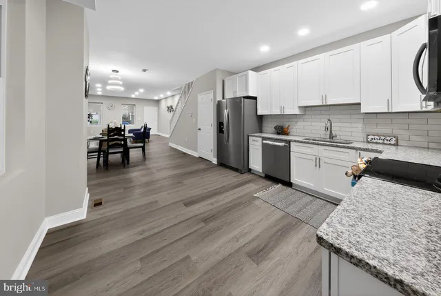 a kitchen with stainless steel appliances granite countertop a stove a refrigerator a sink a dining table and chairs with wooden floor