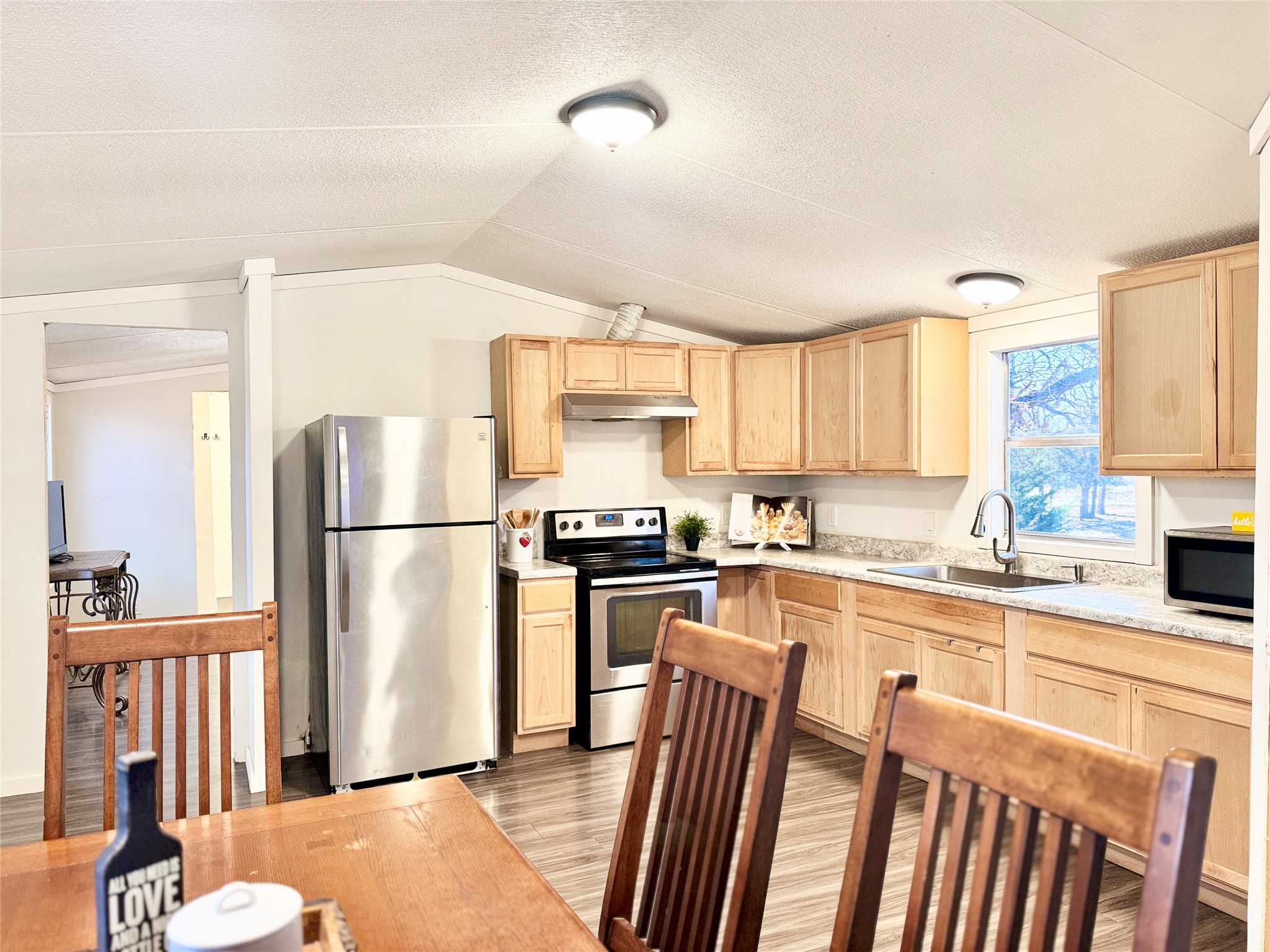 6739 Taylorsville Road Dale, TX 78616 - Photo 11 of 37 Kitchen featuring light wood finish cabinetry, light countertops, stainless steel appliances, light wood-style flooring, and lofted ceiling