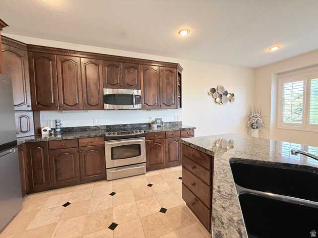 1562 Fairway Ridge Road Draper, UT 84020 - Photo 14 of 60 Kitchen featuring dark wood cabinetry, stainless steel appliances, speckled stone countertops, and a stone tile floor with black accents