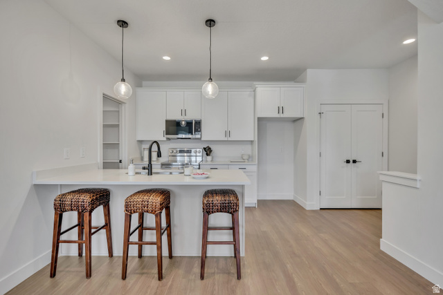 330 East 7635 S Street Sandy, UT 84047 - Photo 6 of 29 Kitchen with a kitchen bar, a peninsula, white cabinetry, stainless steel appliances, and hanging light fixtures