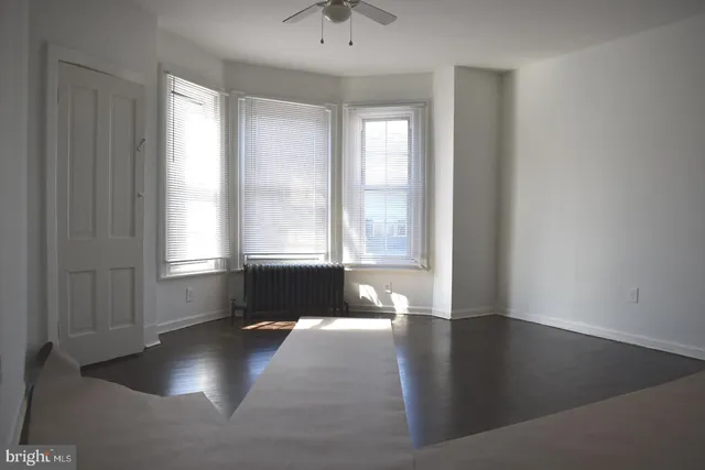 a view of empty room with wooden floor and fan