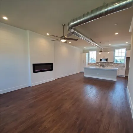an empty room with wooden floor kitchen view and a window