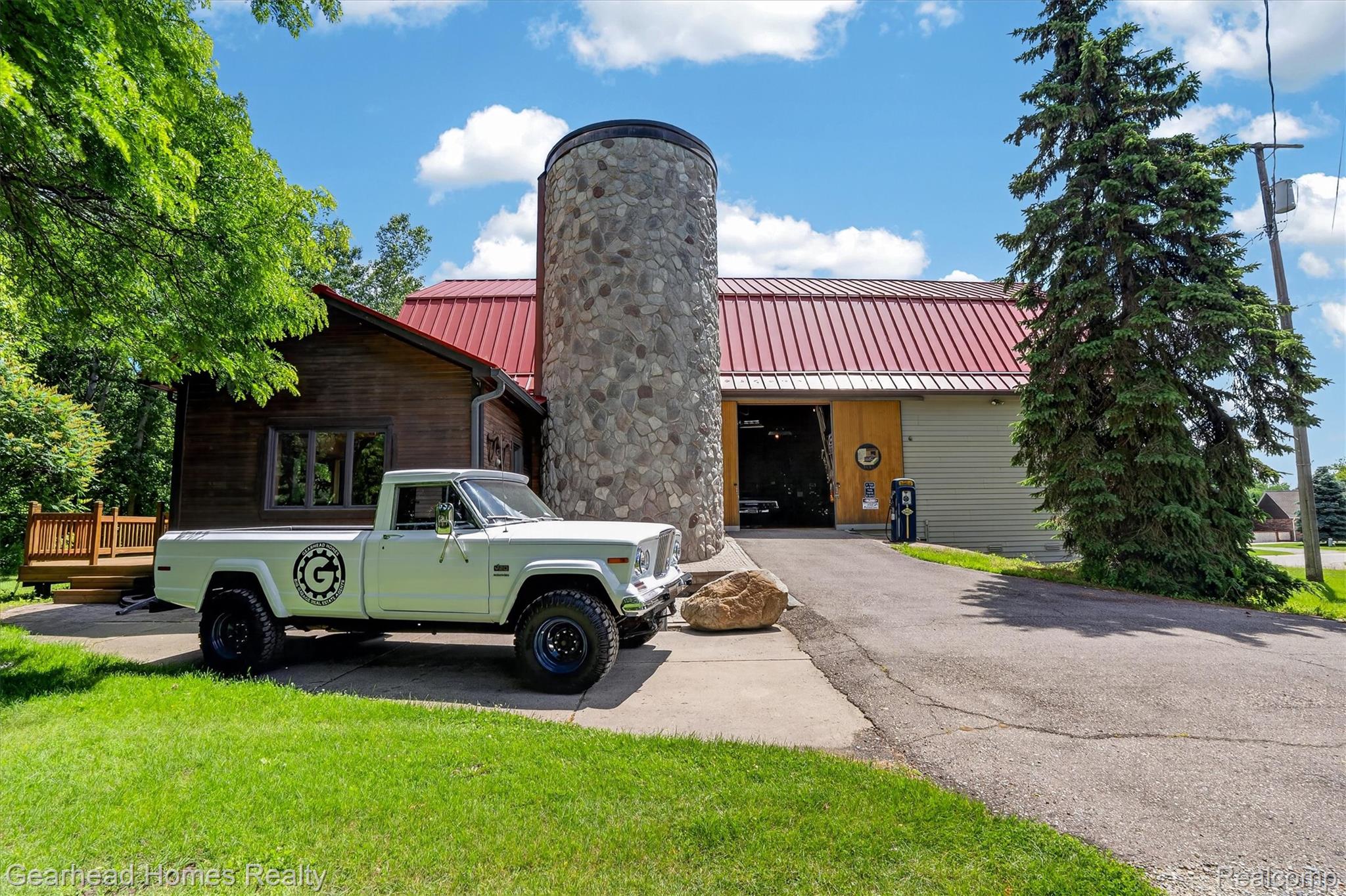 3486 West Drahner Road Oxford, MI 48371 - Photo 35 of 51 Unique architectural design featuring a round stone tower, red metal roofing, wood siding, and an expansive paved driveway