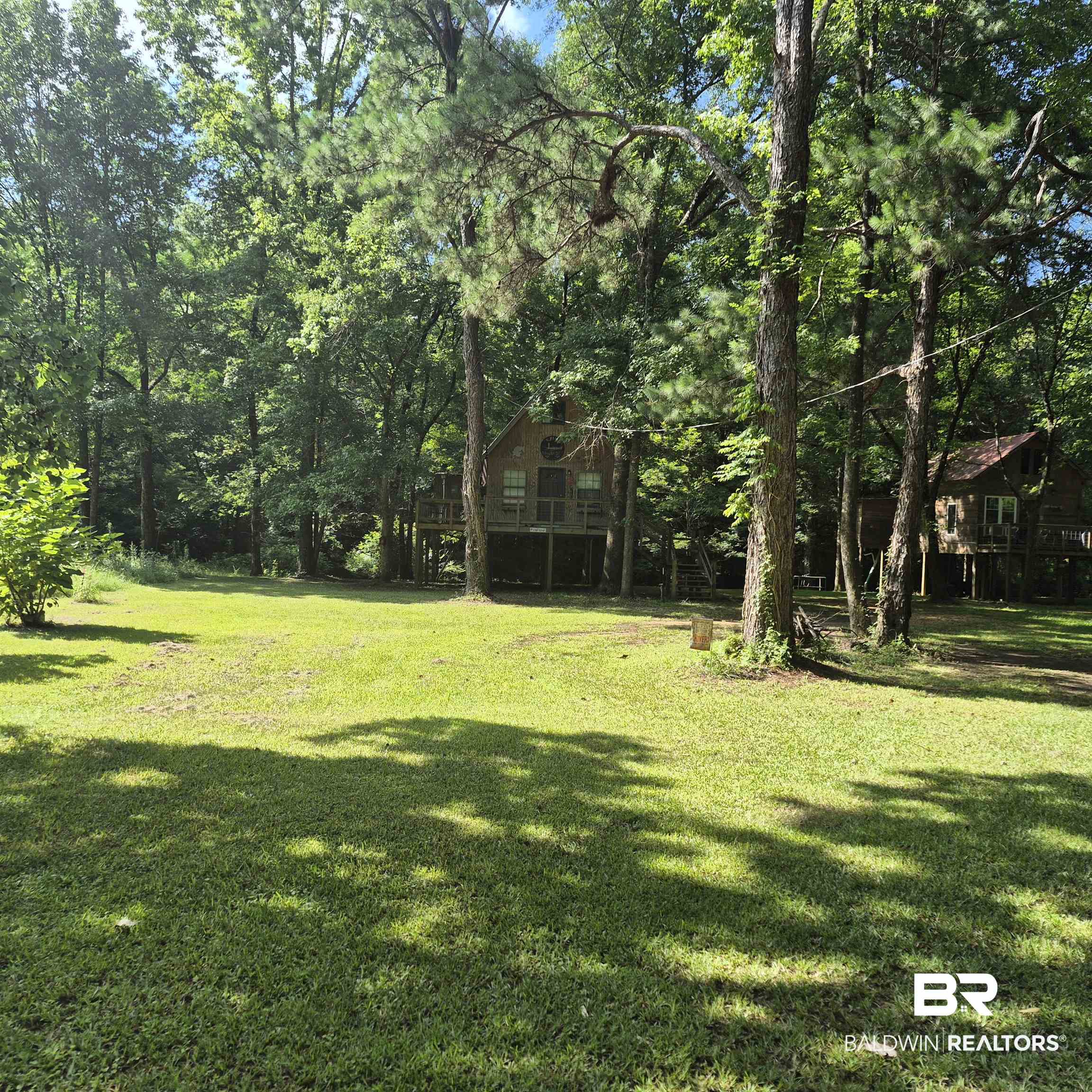 0 Eureka Landing Road Uriah, AL 36480 - Photo 20 of 27 Expansive green lawn surrounded by mature trees, featuring two elevated cabin-style structures with wood siding and decks