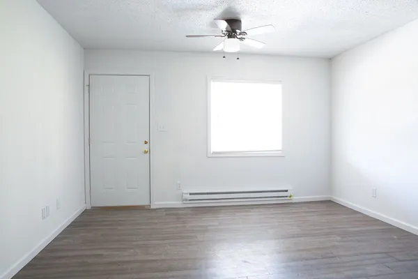 an empty room with wooden floor chandelier fan and windows