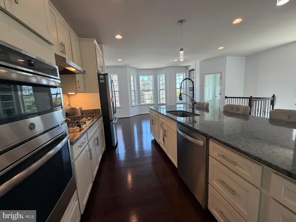 a kitchen with stainless steel appliances granite countertop a refrigerator a stove top oven a dining table and chairs with wooden floor