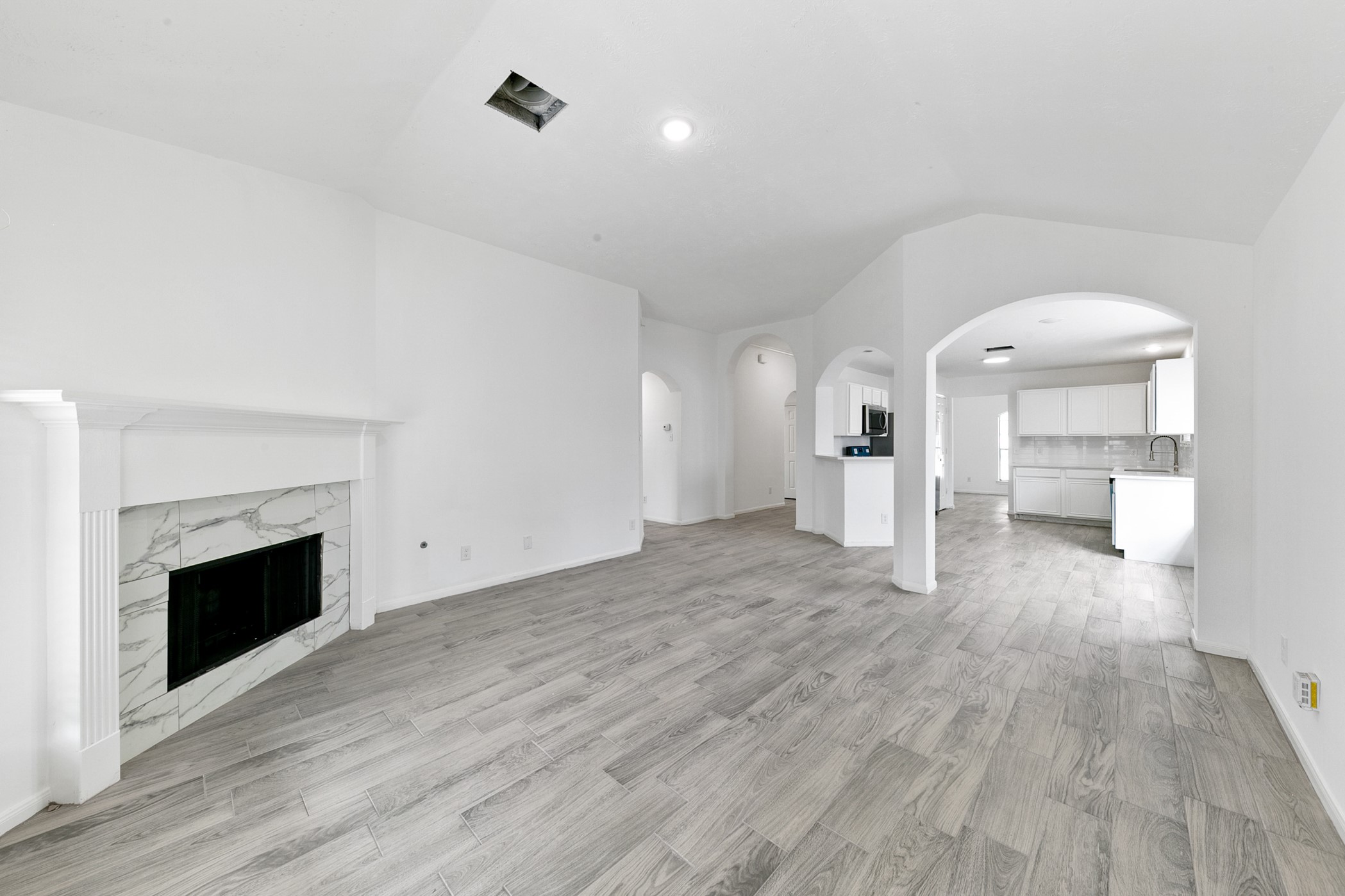 12014 Raven View Drive Houston, TX 77067 - Photo 15 of 29 This spacious interior features an open-concept living area with light wood-style flooring and a cozy fireplace. The room flows seamlessly into a modern kitchen equipped with white cabinetry and stainless steel appliances. Arched doorways add a touch of elegance to the space.