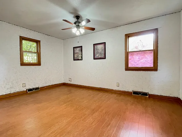 a view of an empty room with chandelier fan and wooden floor