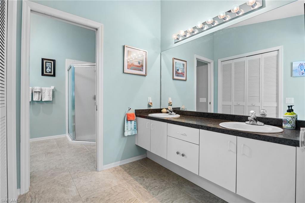 200 St James Way Naples, FL 34104 - Photo 18 of 45 Bathroom featuring a closet, double vanity, a shower stall, and light tile patterned flooring